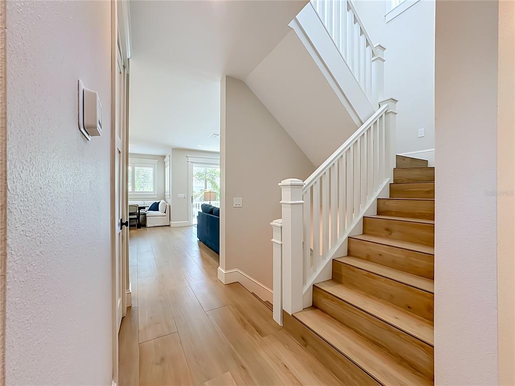 A hallway with light wood flooring leads to a living area beside a wooden staircase — 2918 GULF DRIVE, HOLMES BEACH, FL