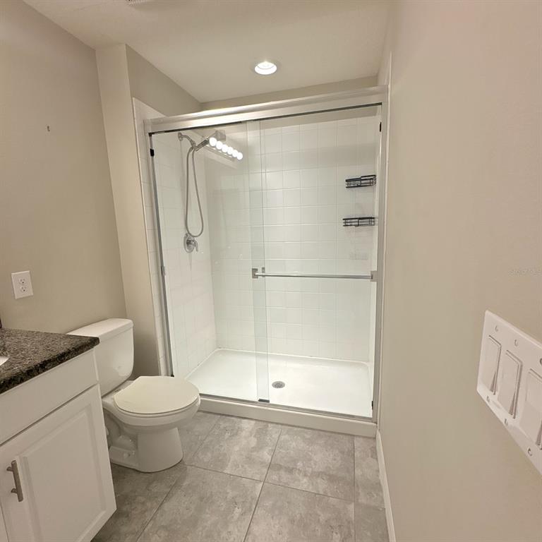A bathroom features a white toilet, a granite-topped vanity, and a tiled shower with glass doors — 7234 GRAND ELM DRIVE, RIVERVIEW, FL