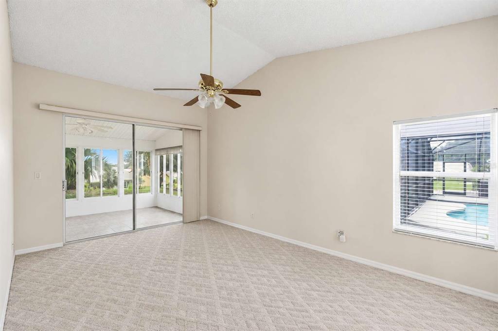 An empty room with beige carpet, a ceiling fan, sliding glass doors, and a window — 24725 BRIGHTWATER COURT, LEESBURG, FL