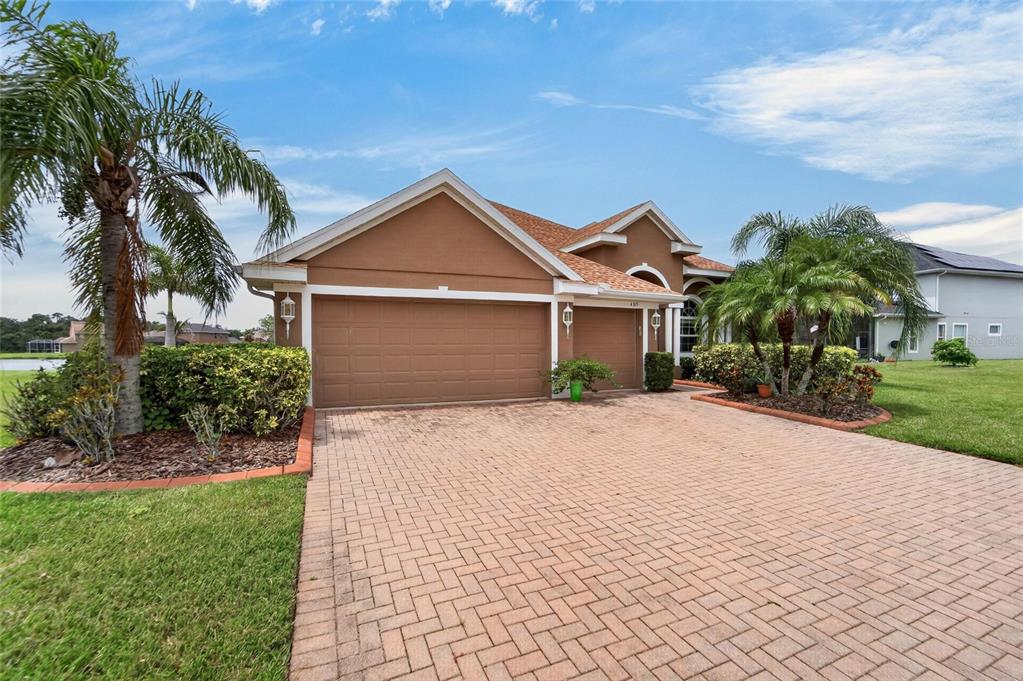 A tan house with a three-car garage and a brick paver driveway under a blue sky — 4315 70TH AVENUE E, ELLENTON, FL