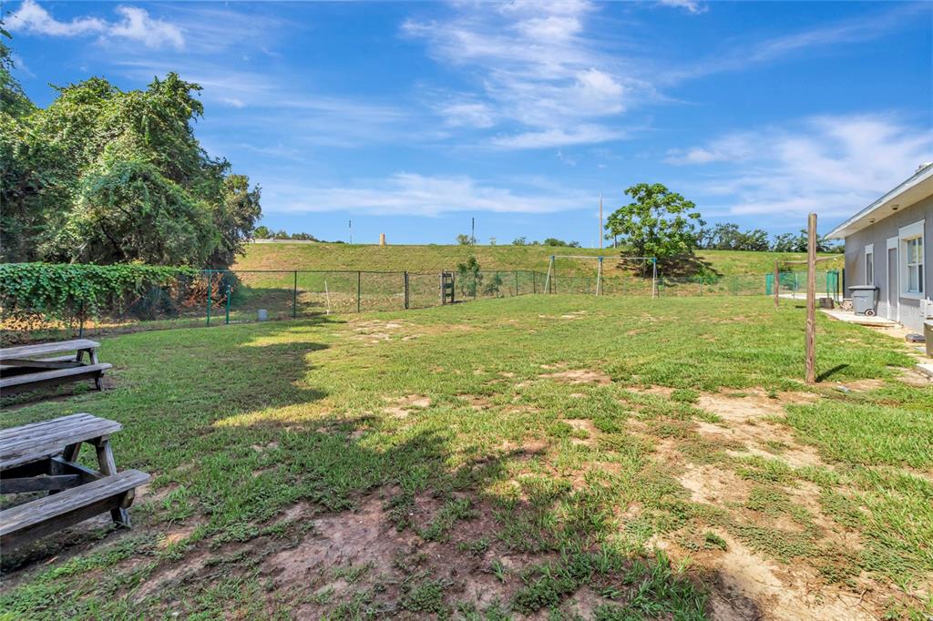A grassy backyard features a chain-link fence, a swing set, and wooden picnic tables — 105 E BAKER STREET, MINNEOLA, FL