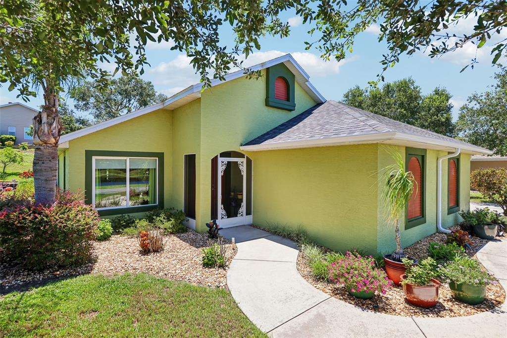 A lime green house with dark green trim, a front walkway, and potted plants — 76 FAIRWAY CIRCLE, UMATILLA, FL