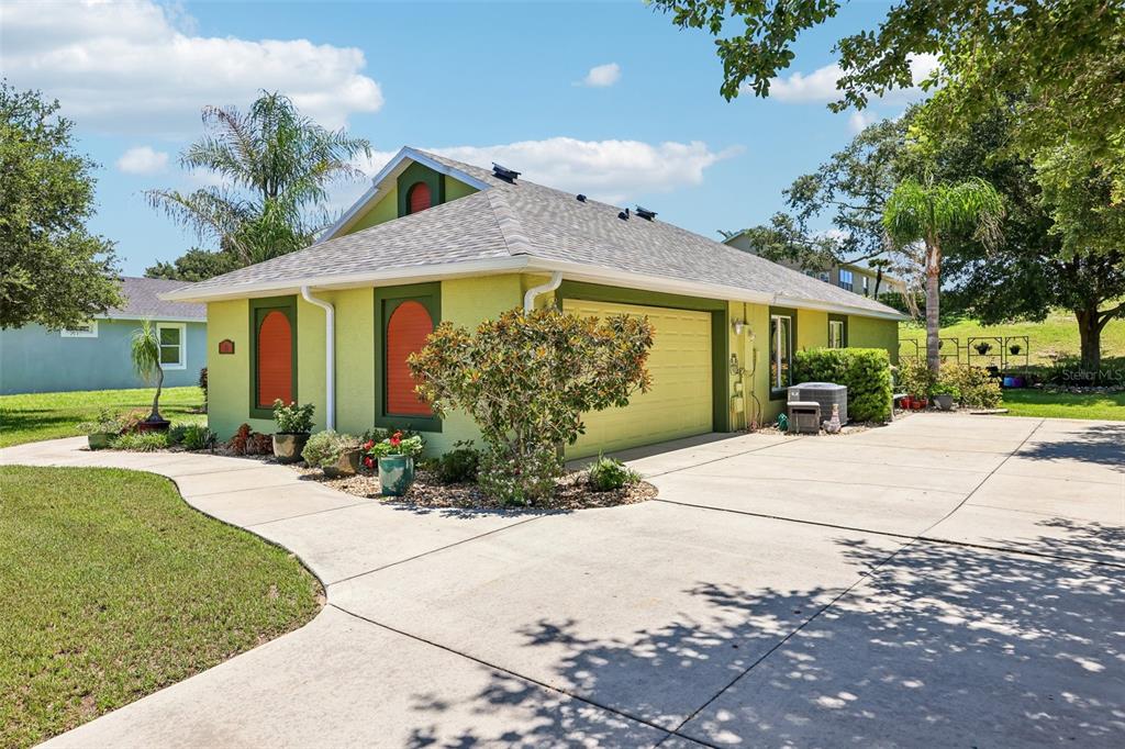 A lime green house with a two-car garage and a concrete driveway under a blue sky — 76 FAIRWAY CIRCLE, UMATILLA, FL