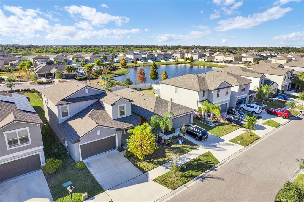 An aerial view shows suburban houses with gray roofs, driveways, and a central pond — 5204 WHITE CHICORY DRIVE, APOLLO BEACH, FL