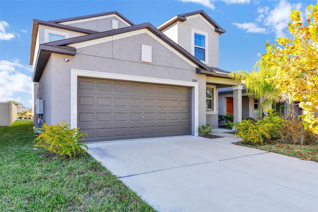 A two-story suburban house features a gray stucco exterior, a two-car garage, and landscaping — 5204 WHITE CHICORY DRIVE, APOLLO BEACH, FL