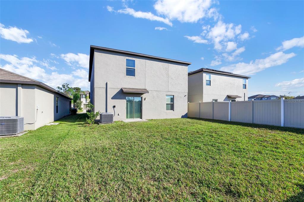 The backyard of a two-story house features a sliding glass door and a vinyl fence — 5204 WHITE CHICORY DRIVE, APOLLO BEACH, FL