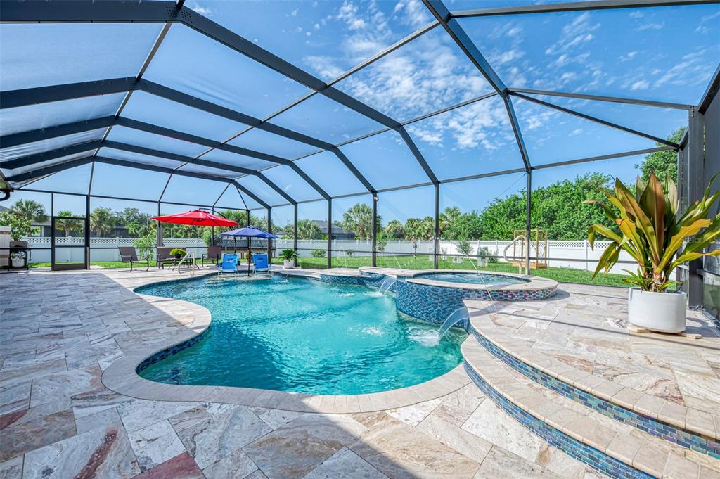 A screened-in pool area features a hot tub with water features and stone patio flooring — 2705 LAMKIN ROAD, NORTH PORT, FL