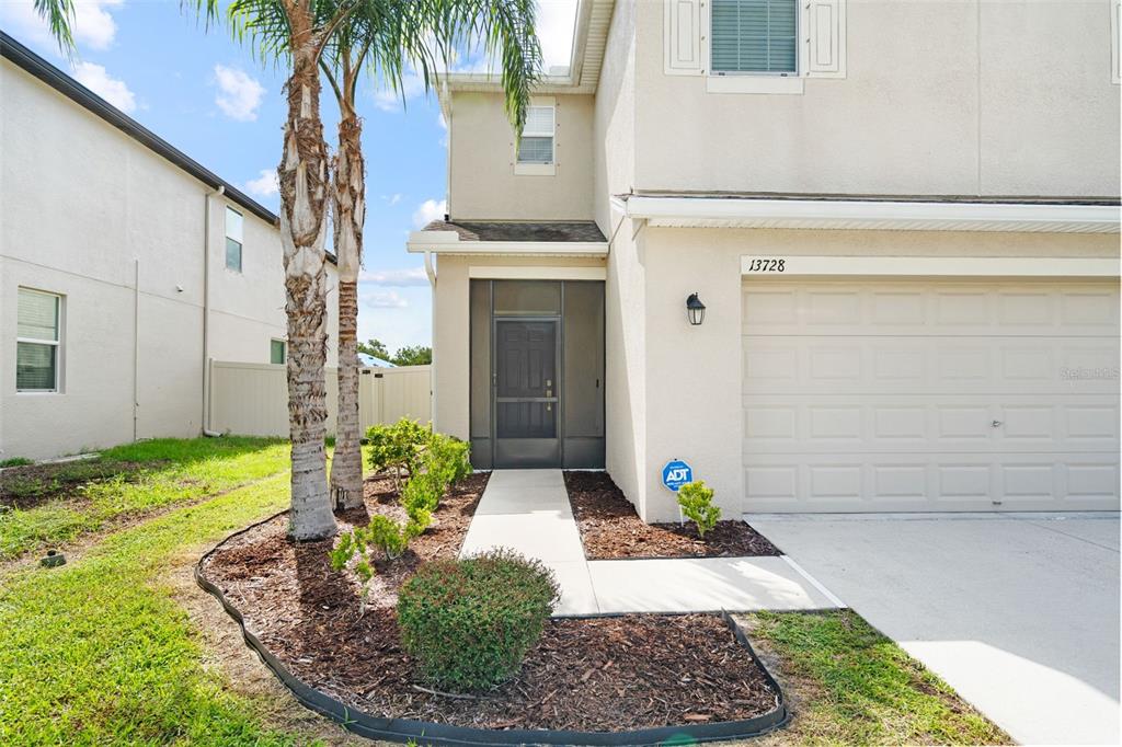 The exterior of a two-story beige house features a garage, a screened entryway, and palm trees — 13728 REINDEER CIRCLE, HUDSON, FL