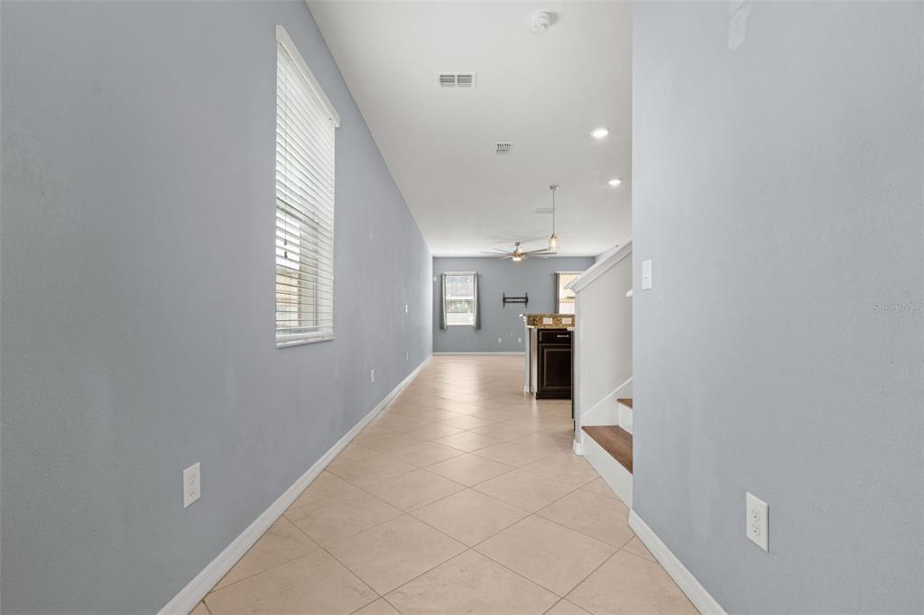 A long hallway with light-colored tile flooring leads toward an open-concept kitchen and living area — 13728 REINDEER CIRCLE, HUDSON, FL