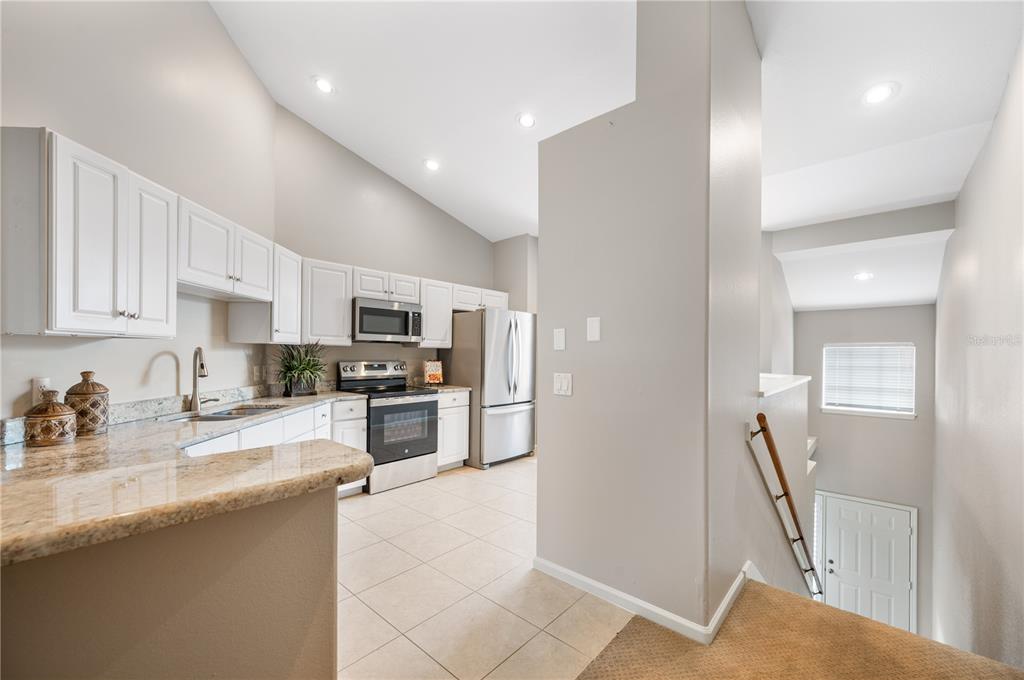 A kitchen with white cabinets, granite countertops, and stainless steel appliances overlooks a carpeted staircase — 411 ENCLAVE PLACE UNIT 411, LAKELAND, FL