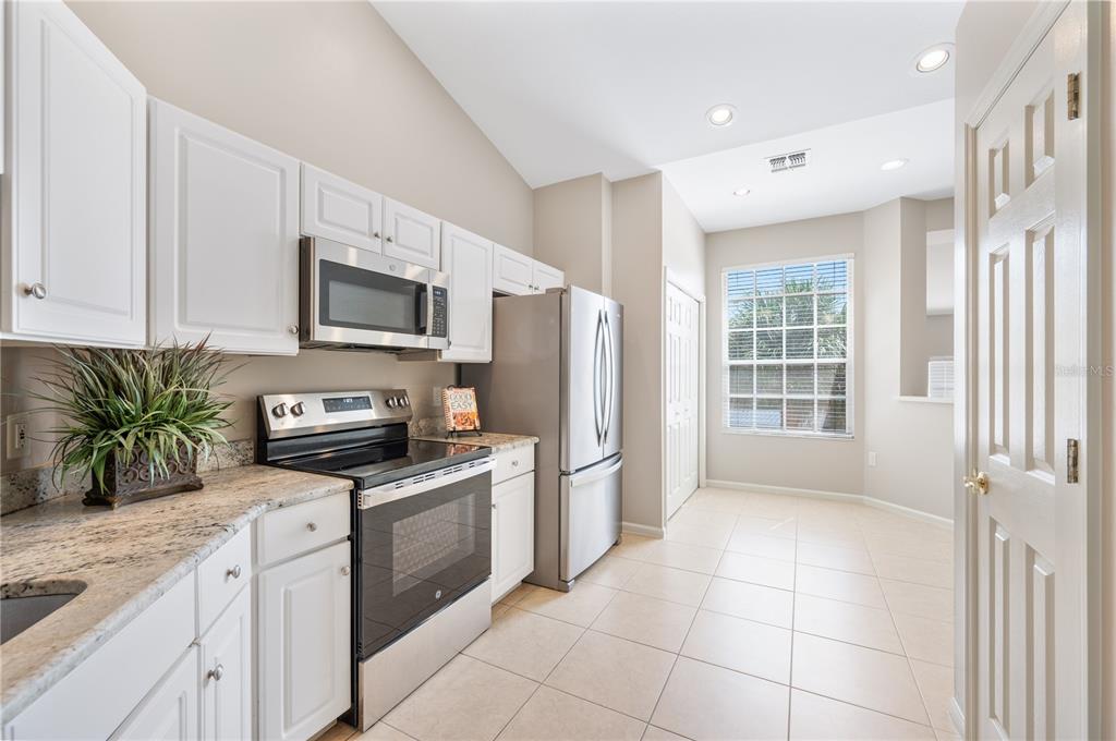 A kitchen with white cabinets, stainless steel appliances, granite countertops, and tile flooring — 411 ENCLAVE PLACE UNIT 411, LAKELAND, FL