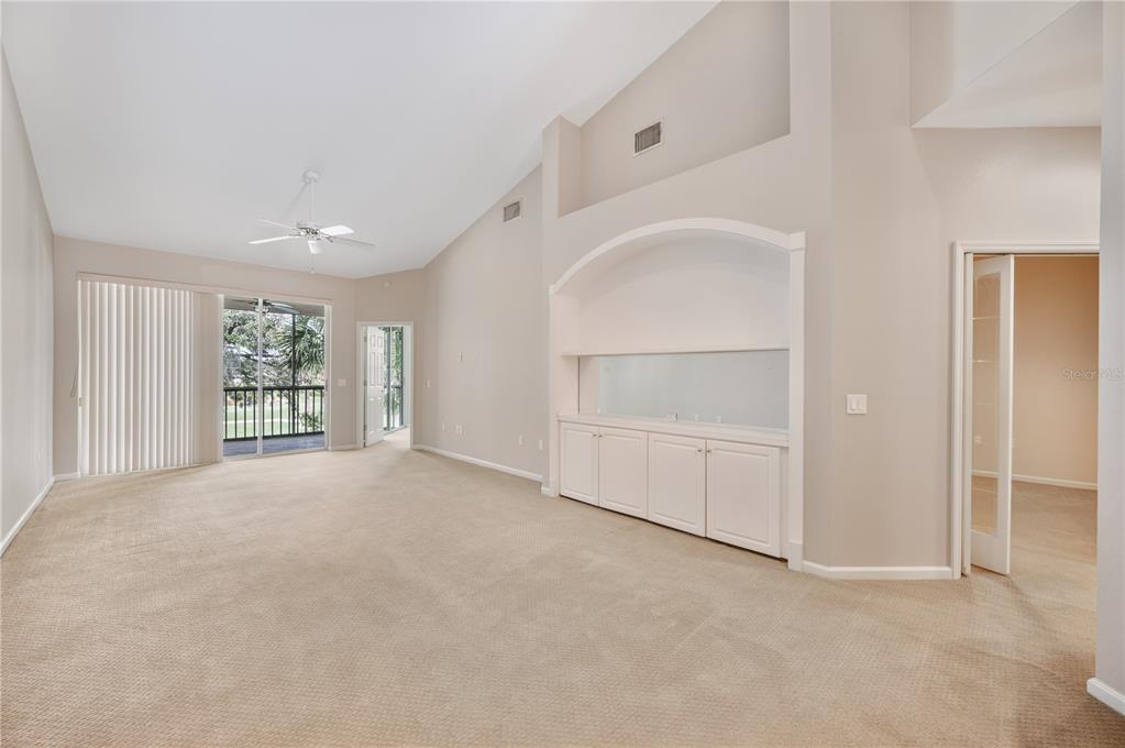A carpeted living room features a vaulted ceiling, a built-in cabinet, and a sliding glass door — 411 ENCLAVE PLACE UNIT 411, LAKELAND, FL