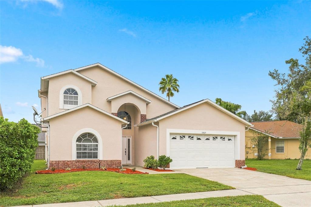 A two-story, light-colored stucco house with a two-car garage and a front lawn — 12827 DOWNSTREAM CIRCLE, ORLANDO, FL