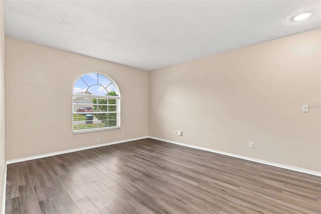 An empty bedroom features beige walls, wood-look flooring, and an arched window with blinds — 12827 DOWNSTREAM CIRCLE, ORLANDO, FL