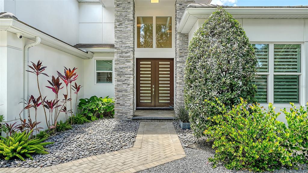 A stone-accented entryway features a double door, a paved walkway, and various landscaping plants — 1838 OLEANDER STREET, SARASOTA, FL