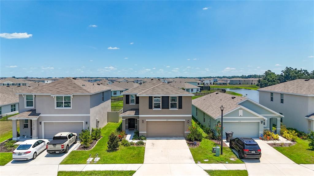 Three suburban houses with driveways and lawns are shown under a clear blue sky — 12142 MOUNTAIN ISLAND TRAIL, PARRISH, FL