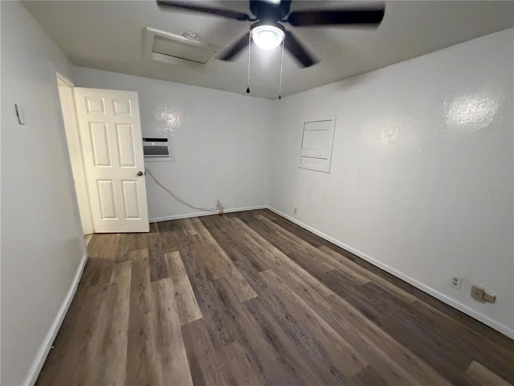 An empty bedroom features white walls, wood-look flooring, a ceiling fan, and a wall-mounted air conditioner — 410 W HOWRY AVENUE UNIT D, DELAND, FL