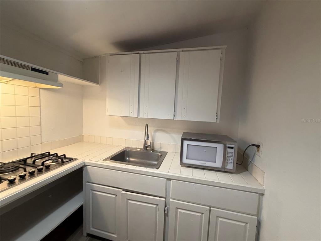 A kitchen features white cabinets, a tiled countertop, a stainless steel sink, and a microwave — 410 W HOWRY AVENUE UNIT D, DELAND, FL