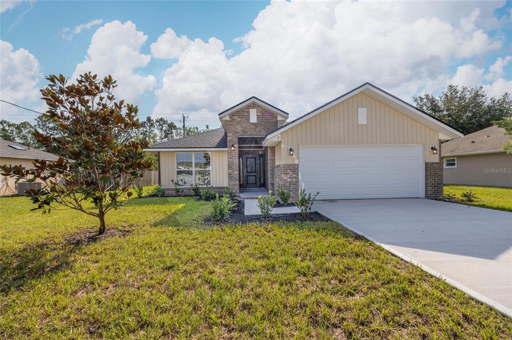 A single-story house with a brick entryway, tan vertical siding, and a two-car garage — 7 ZIRCON COURT, PALM COAST, FL