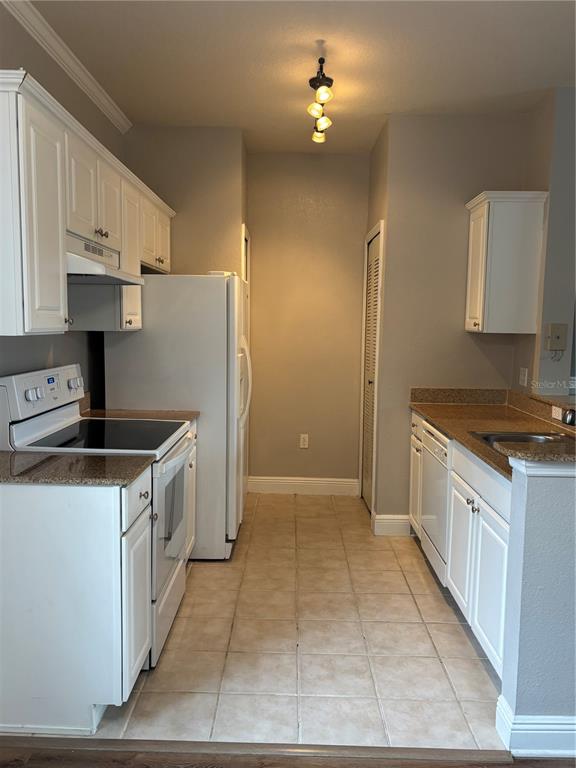 A galley kitchen features white cabinets, white appliances, tan tile flooring, and granite countertops — 213 SOUTHERN PECAN CIRCLE UNIT 201, WINTER GARDEN, FL