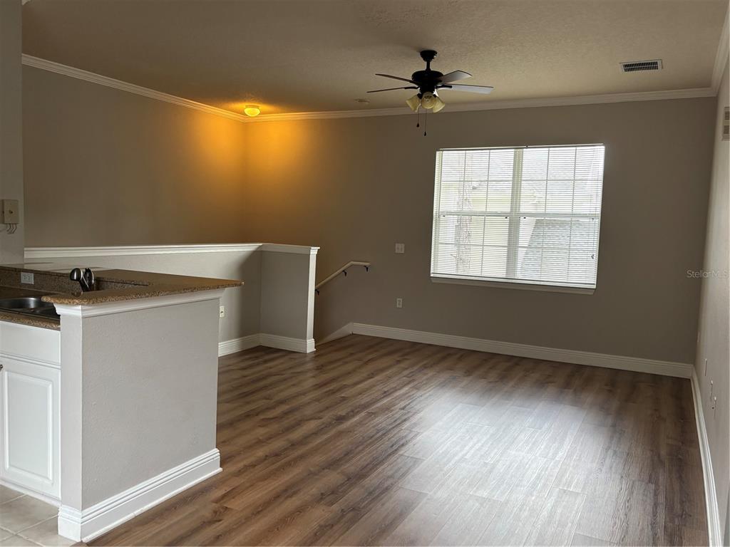 An open-concept living area features wood-look flooring, a ceiling fan, and a kitchen peninsula — 213 SOUTHERN PECAN CIRCLE UNIT 201, WINTER GARDEN, FL