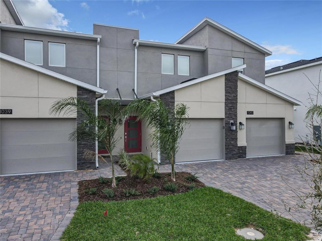 A two-story townhouse exterior features gray stucco, stone accents, two garages, and a paved driveway — 1041 SPLASH SHOT PLACE UNIT 1041, DAVENPORT, FL