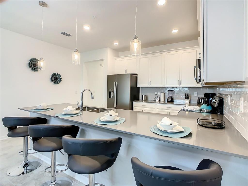 A kitchen features a gray island with bar stools, white cabinets, and stainless steel appliances — 1041 SPLASH SHOT PLACE UNIT 1041, DAVENPORT, FL