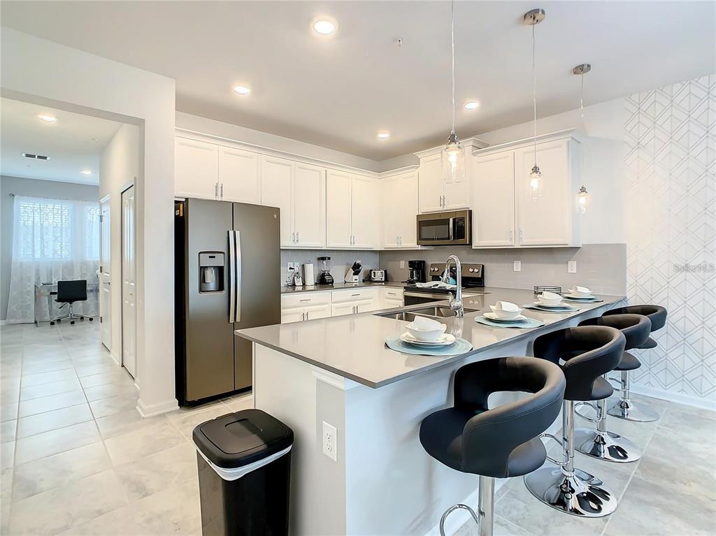 A modern kitchen features white cabinetry, gray countertops, a center island, and black bar stools — 1041 SPLASH SHOT PLACE UNIT 1041, DAVENPORT, FL
