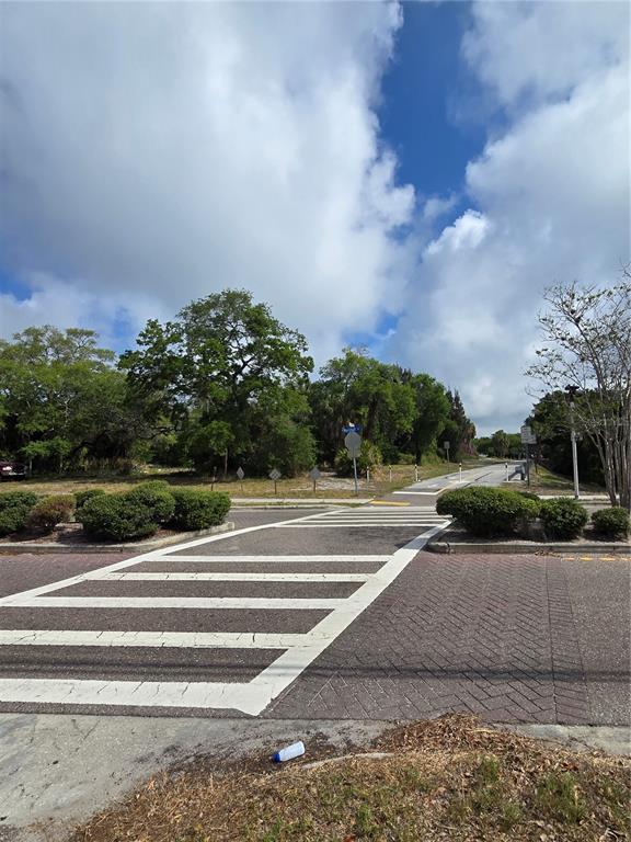 A paved crosswalk leads toward a road lined with trees under a cloudy blue sky — 000 MARSHALL STREET, CLEARWATER, FL