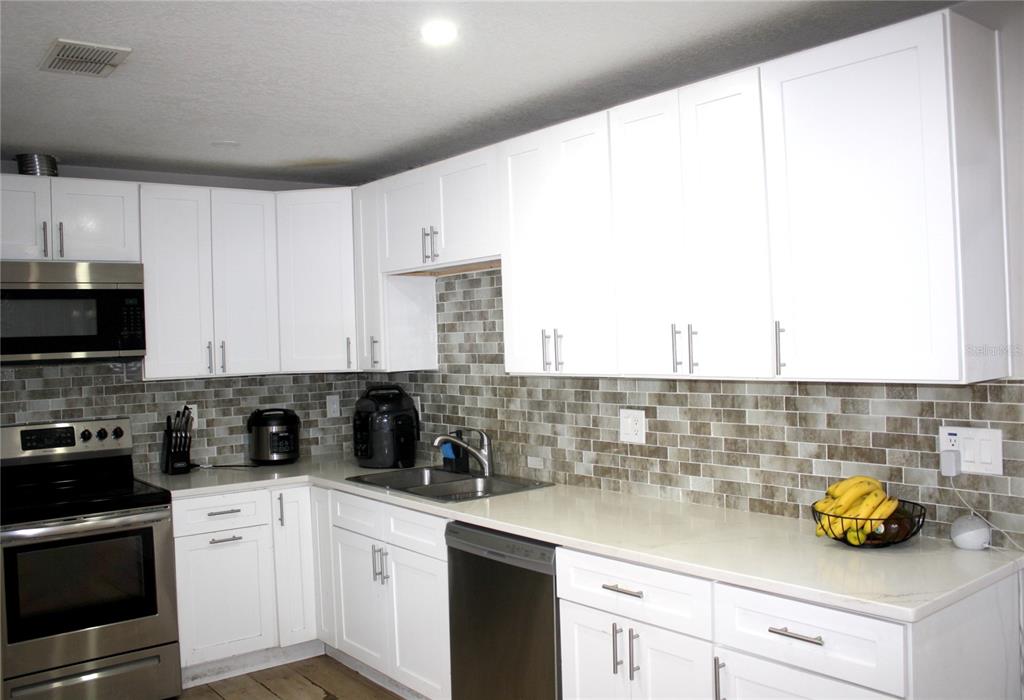 A kitchen features white shaker cabinets, stainless steel appliances, and a brown tiled backsplash — 3620 N 56TH STREET, TAMPA, FL