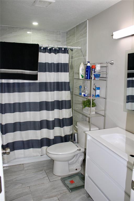 A bathroom features a striped shower curtain, a toilet, a metal shelving unit, and a vanity — 3620 N 56TH STREET, TAMPA, FL
