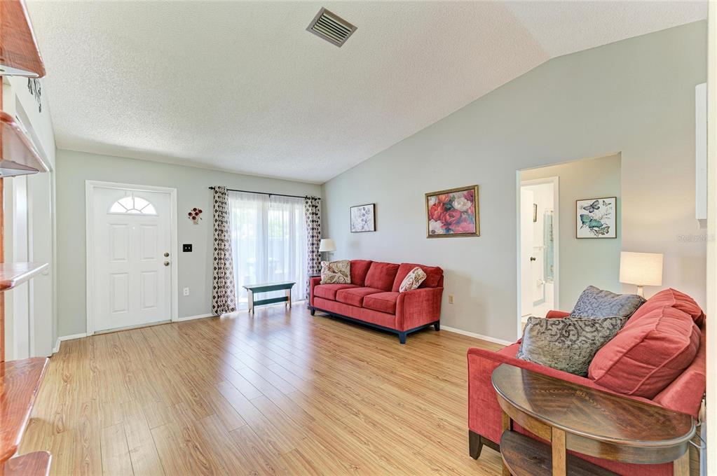 A living room features wood-look flooring, a vaulted ceiling, and two red sofas — 3403 36TH STREET W UNIT 109, BRADENTON, FL