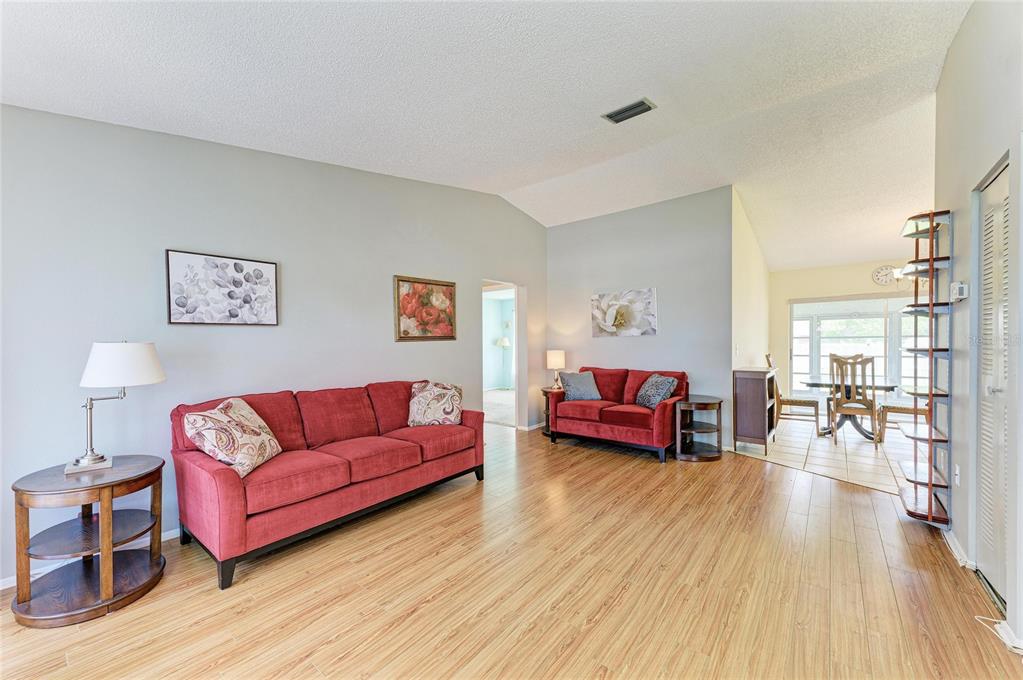 A living room features red sofas, wood-look flooring, and an adjacent dining area — 3403 36TH STREET W UNIT 109, BRADENTON, FL