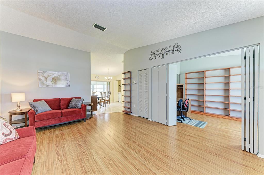 A living room with wood-look flooring, a red sofa, and an adjacent room with shelving — 3403 36TH STREET W UNIT 109, BRADENTON, FL