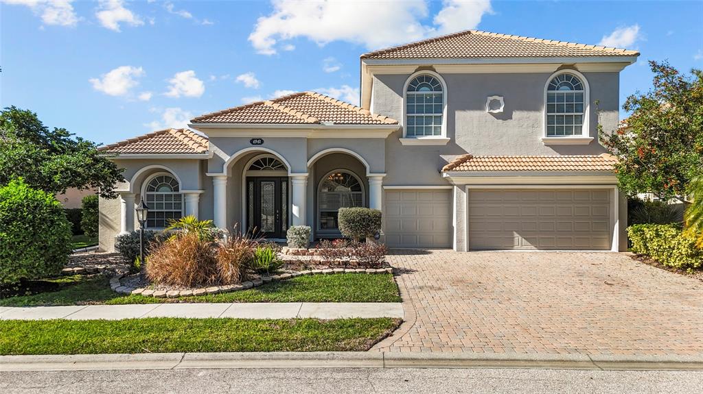 A two-story house with a beige stucco exterior, tiled roof, and a paved driveway — 6961 SCRUB JAY DRIVE, SARASOTA, FL