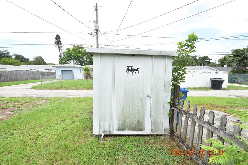 A weathered, light-colored storage shed stands in a grassy yard near a wooden fence — 5124 18TH AVENUE N, ST PETERSBURG, FL