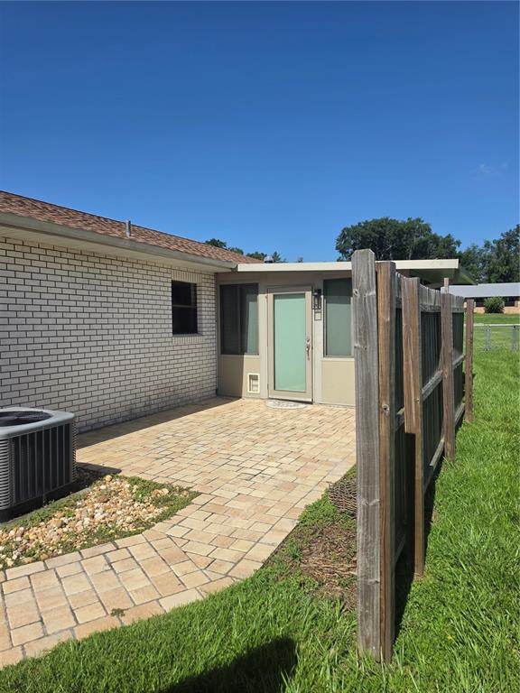 A brick house exterior features a paved patio, a glass-paneled door, and a wooden fence — 7315 SE 109TH PLACE, BELLEVIEW, FL