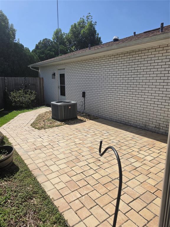 A brick house exterior features a paved patio, an air conditioning unit, and a wooden fence — 7315 SE 109TH PLACE, BELLEVIEW, FL