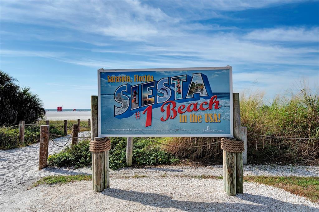 A sign for Siesta Beach stands on a sandy path surrounded by dunes and vegetation — 5640 CAPE LEYTE DRIVE, SARASOTA, FL