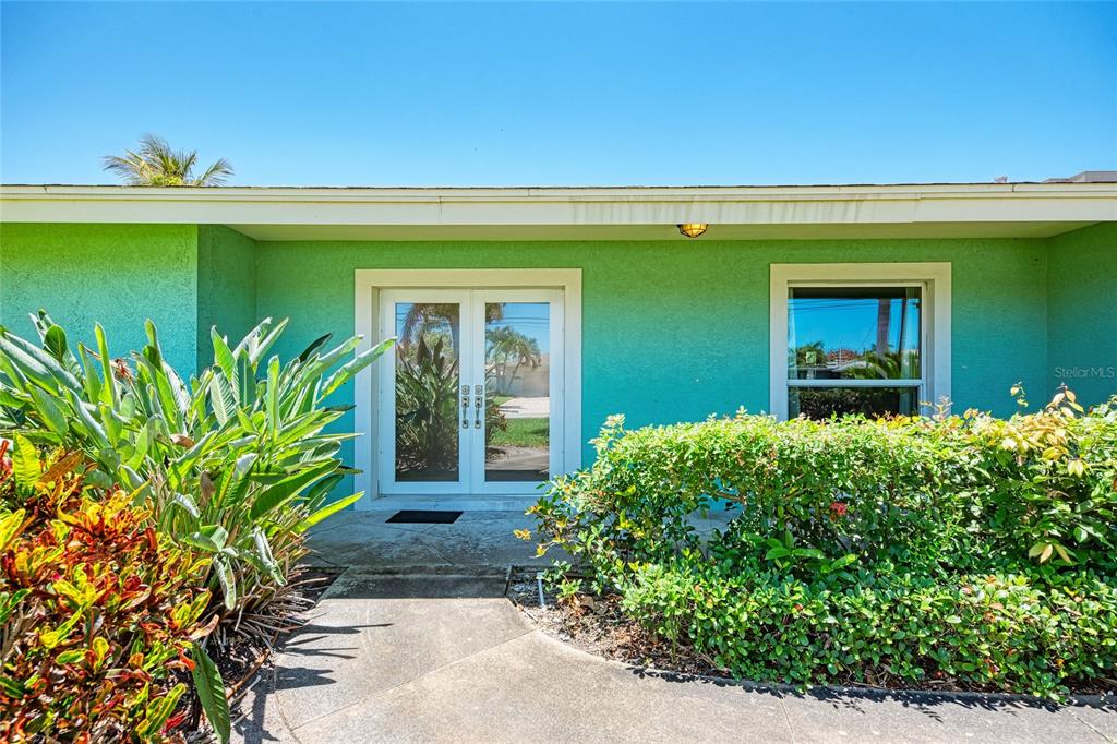 The exterior of a house features a bright green facade, double glass doors, and landscaping — 5640 CAPE LEYTE DRIVE, SARASOTA, FL