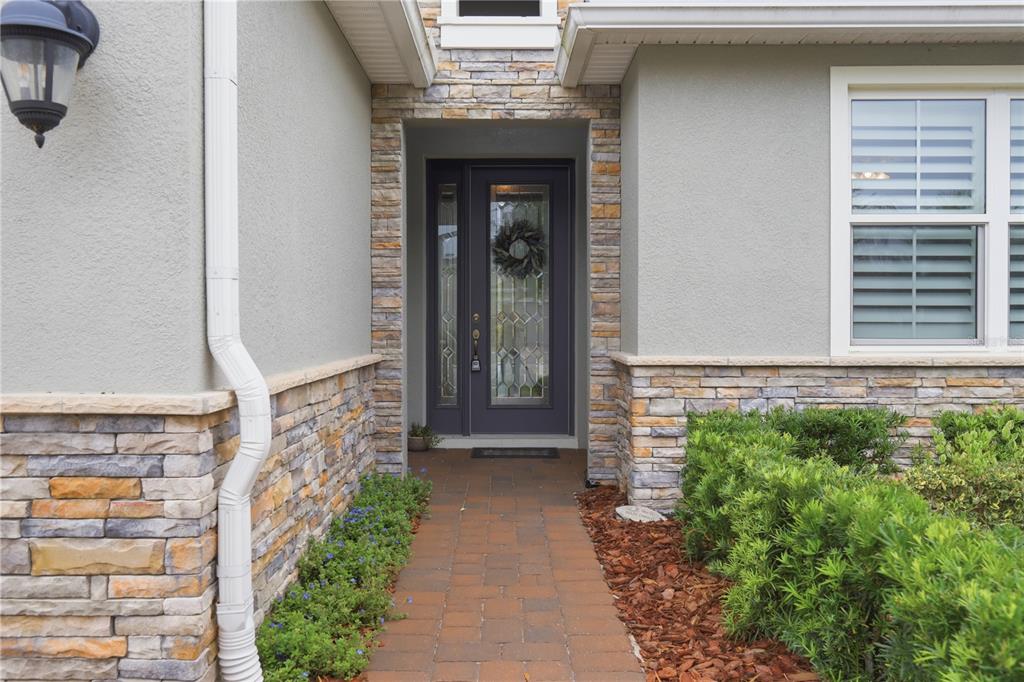 A stone-accented entryway features a dark front door with glass panels and a brick walkway — 261 OLD MOSS CIRCLE, DELAND, FL