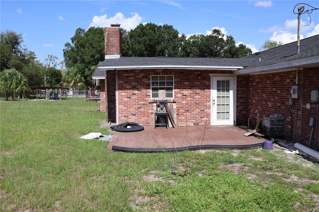 A brick house exterior features a small patio, a chimney, and a white glass-paneled door — 699 BAKER STREET, WAUCHULA, FL