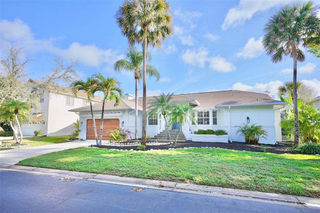 A white single-story house with a wooden garage door and palm trees in the front yard — 4717 E TRAILS DRIVE, SARASOTA, FL