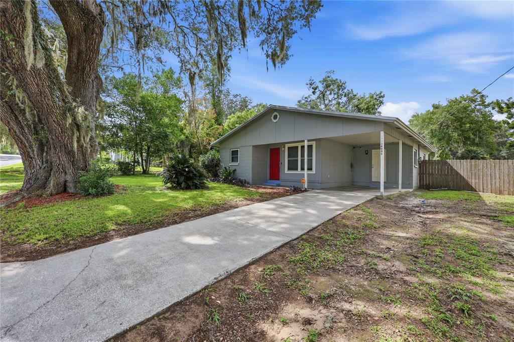 A single-story gray house with a red front door, a carport, and a large oak tree — 14004 NW 158TH AVENUE, ALACHUA, FL