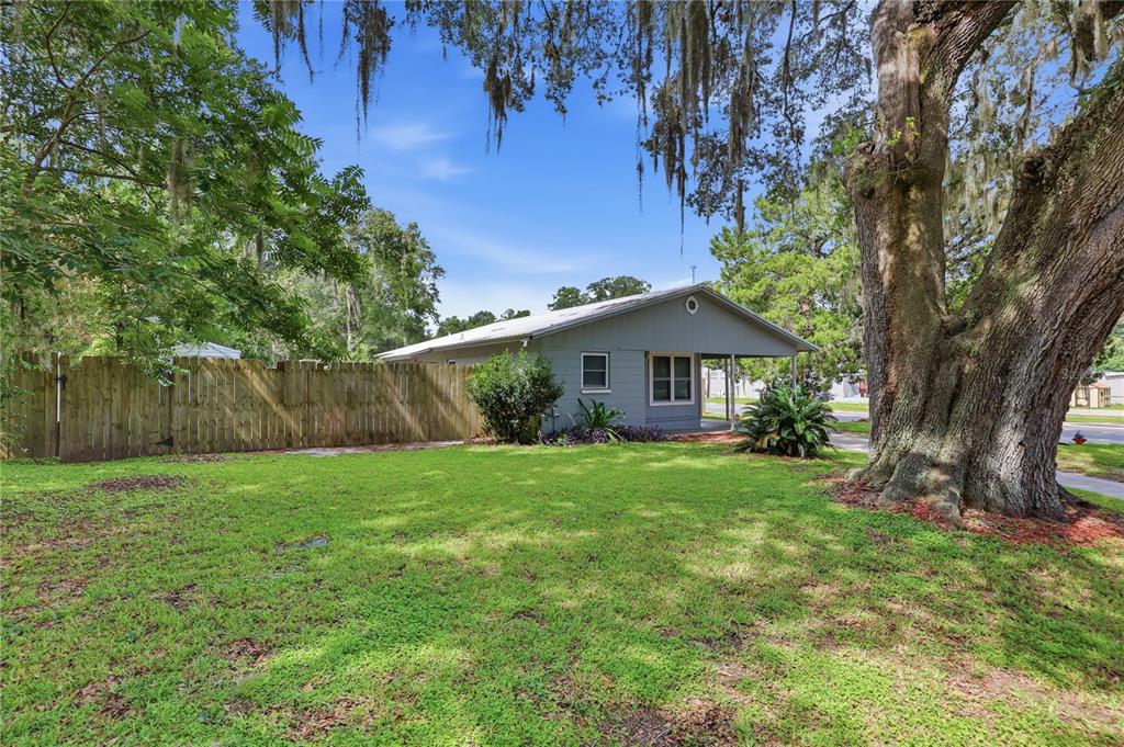 A gray house with a metal roof sits behind a wooden fence and large tree — 14004 NW 158TH AVENUE, ALACHUA, FL