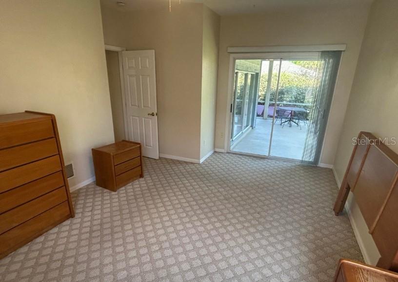 A bedroom with carpeted flooring, wooden furniture, and a sliding glass door leading to a patio — 38 MAGNOLIA DRIVE S UNIT 38, ORMOND BEACH, FL