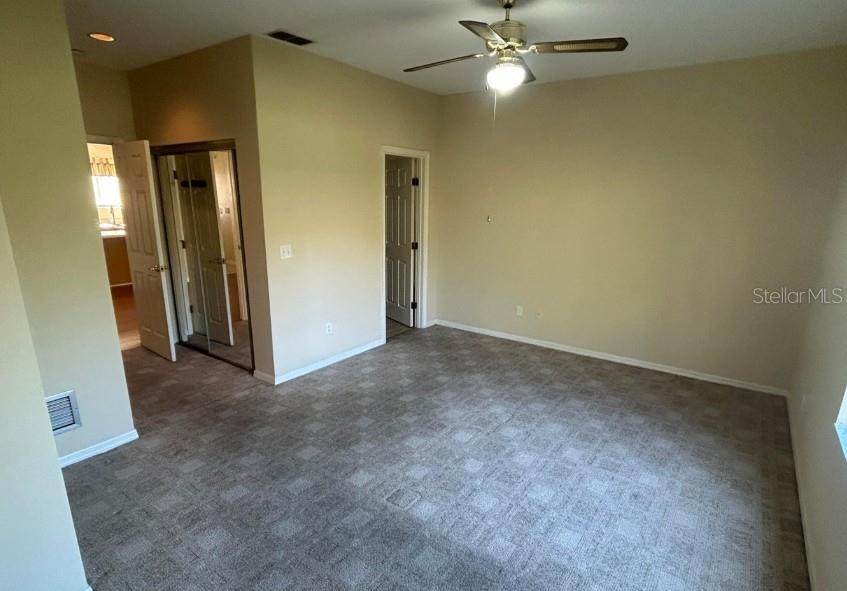 A bedroom features beige walls, gray patterned carpet, a ceiling fan, and two interior doors — 38 MAGNOLIA DRIVE S UNIT 38, ORMOND BEACH, FL