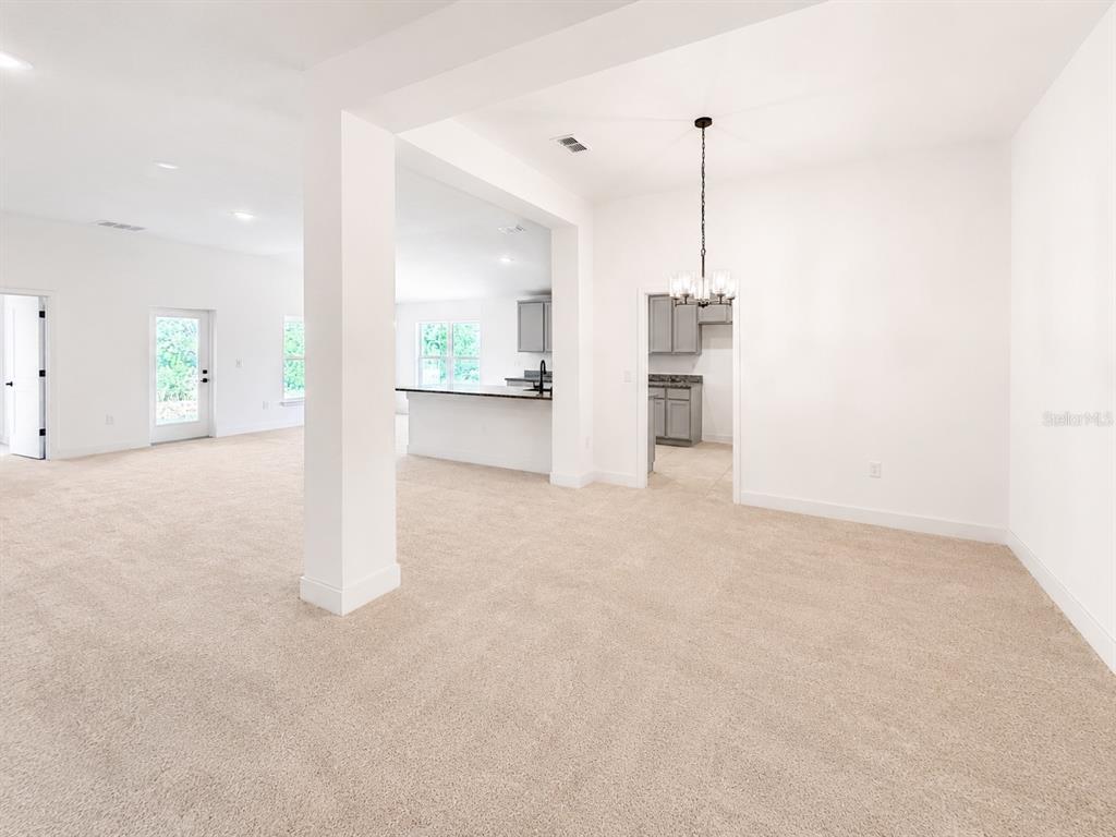 An open-concept living area with beige carpet, white walls, and a view into the kitchen — 7636 BENT TREE LOOP, ST CLOUD, FL
