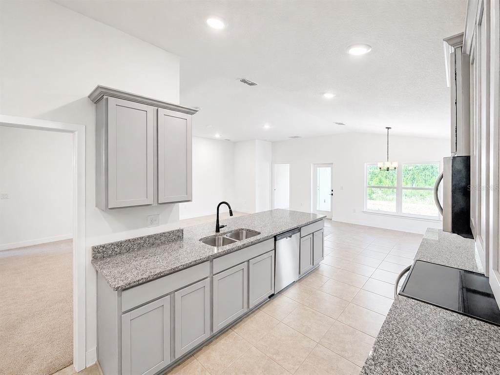 A kitchen features gray cabinets, granite countertops, a stainless steel dishwasher, and tile flooring — 7636 BENT TREE LOOP, ST CLOUD, FL