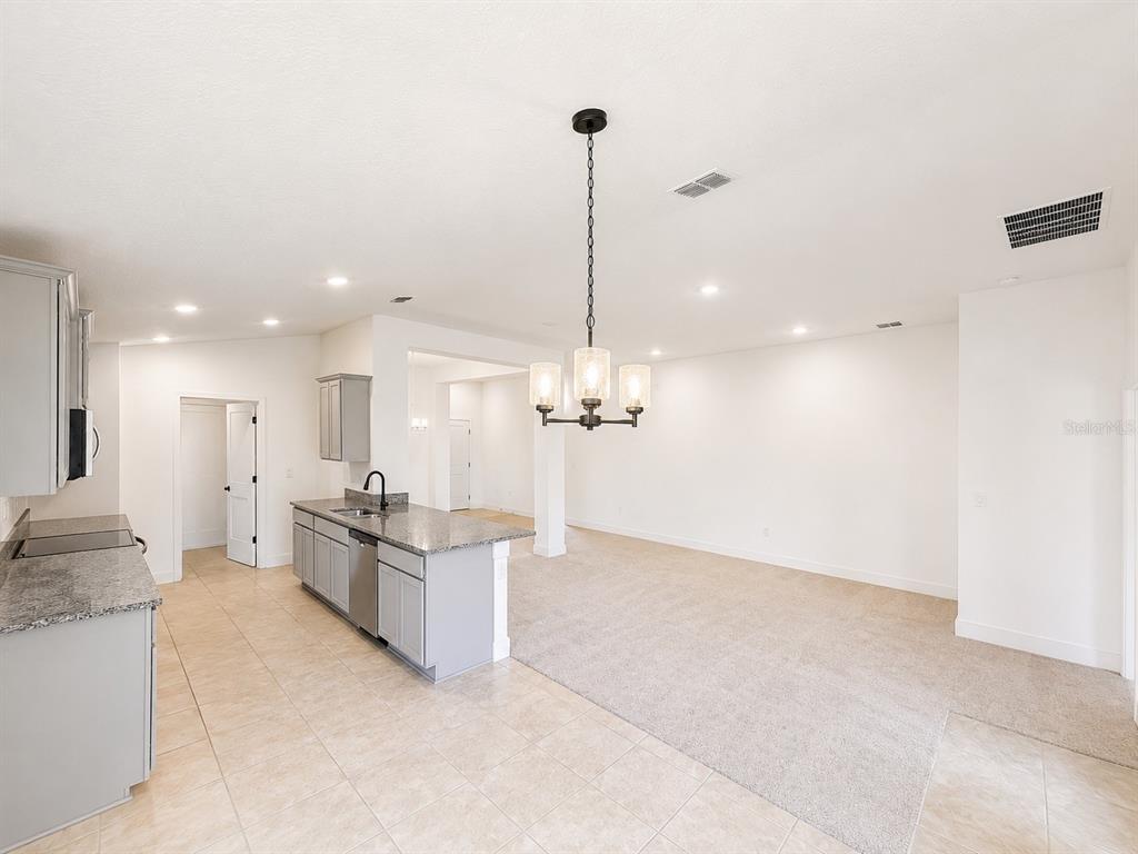 A kitchen with gray cabinets and granite countertops opens into a carpeted dining area — 7636 BENT TREE LOOP, ST CLOUD, FL